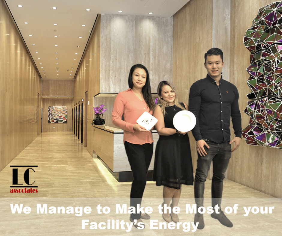 LC Associates Three individuals stand in a polished hallway with wooden walls and a modern decor. They hold various devices related to energy management. The text reads, "We Manage to Make the Most of your Facility’s Energy." The logo "LC Associates" is visible on the left. Con Edison Cash Incentives